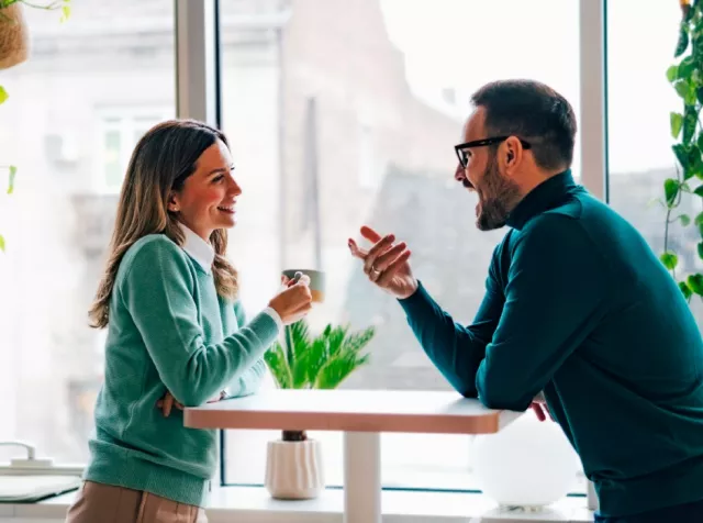two colleagues, a man and a woman leaning over a tall table chatting while having a coffee 